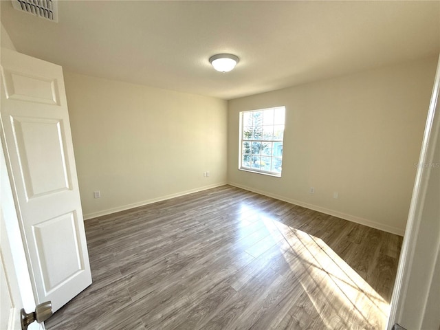 unfurnished room featuring dark wood-type flooring, visible vents, and baseboards