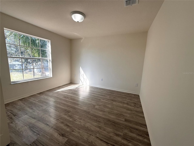 spare room featuring dark wood-style flooring, visible vents, and baseboards