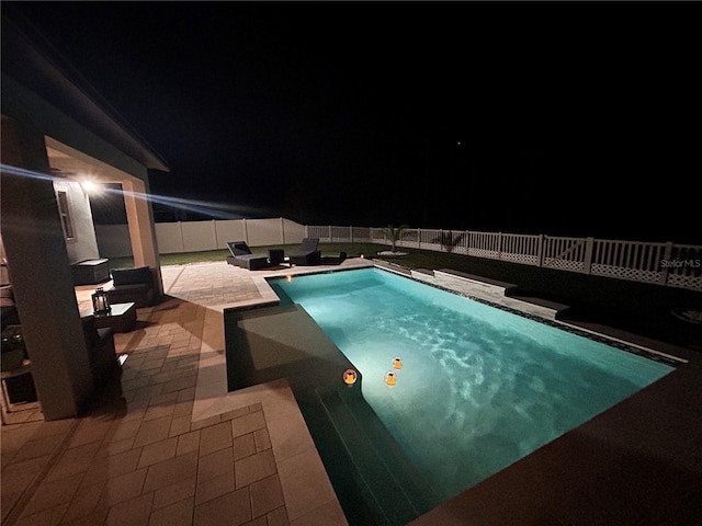 pool at night featuring a patio area