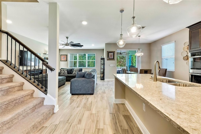 kitchen with sink, light hardwood / wood-style flooring, ceiling fan, light stone countertops, and decorative light fixtures