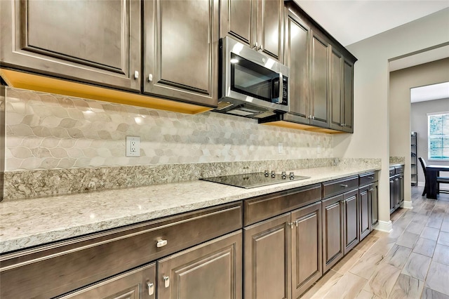 kitchen featuring backsplash, dark brown cabinetry, black electric cooktop, and light stone counters