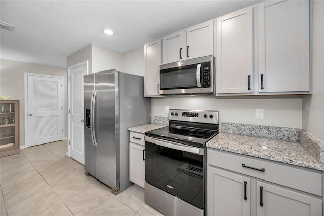 kitchen with light stone countertops, a textured ceiling, stainless steel appliances, light tile patterned floors, and white cabinets