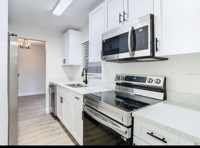 kitchen featuring white cabinetry, sink, stainless steel appliances, light hardwood / wood-style floors, and a textured ceiling