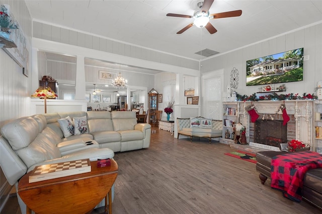 living room featuring a fireplace, hardwood / wood-style floors, ceiling fan with notable chandelier, and crown molding