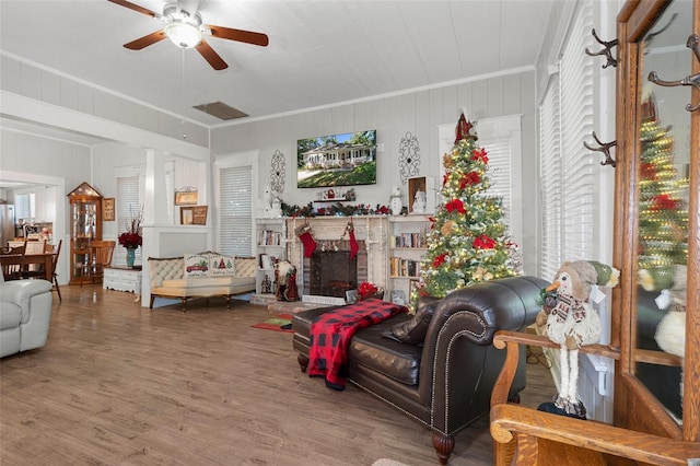 living room featuring wooden walls, hardwood / wood-style flooring, ceiling fan, ornamental molding, and a fireplace