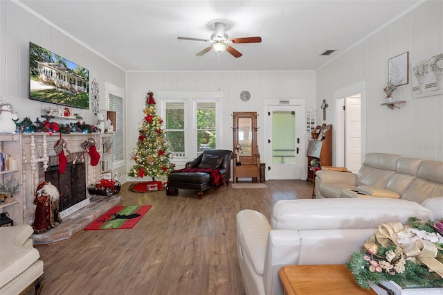 living room with hardwood / wood-style flooring, ceiling fan, wood walls, and ornamental molding