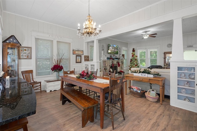 dining room with hardwood / wood-style floors, ceiling fan with notable chandelier, ornamental molding, and wooden walls