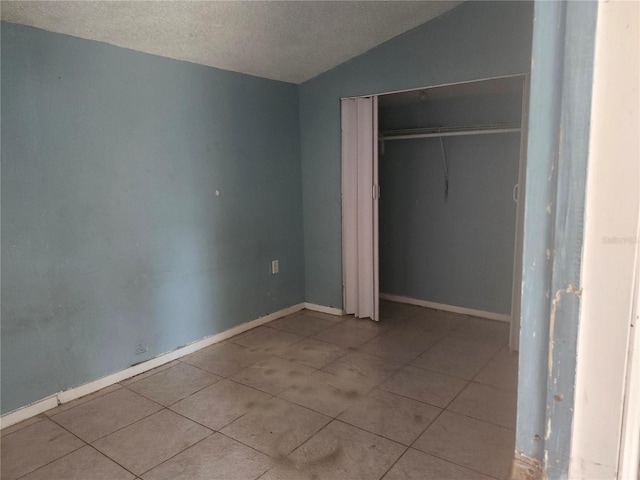 unfurnished bedroom with a textured ceiling, a closet, light tile patterned flooring, and lofted ceiling