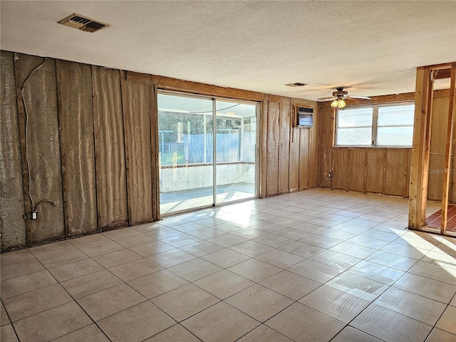 tiled spare room with a textured ceiling, ceiling fan, and wooden walls