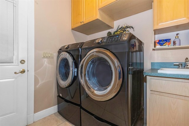 laundry area featuring washing machine and clothes dryer, sink, light tile patterned floors, and cabinets