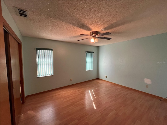 unfurnished bedroom featuring ceiling fan, a closet, wood-type flooring, and multiple windows