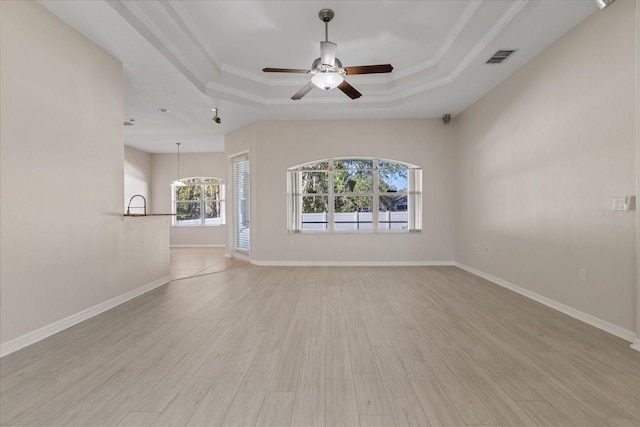 unfurnished living room with a tray ceiling, ceiling fan, light hardwood / wood-style flooring, and ornamental molding