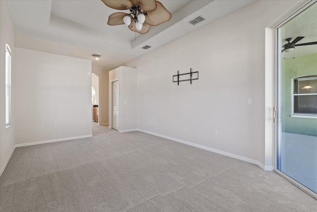 carpeted spare room featuring a raised ceiling and ceiling fan