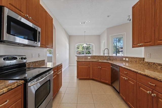 kitchen with sink, hanging light fixtures, light tile patterned floors, light stone countertops, and stainless steel appliances