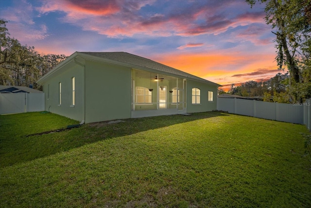 back house at dusk with ceiling fan and a lawn