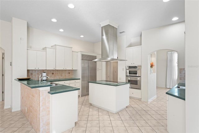 kitchen with sink, stainless steel appliances, kitchen peninsula, island range hood, and white cabinets