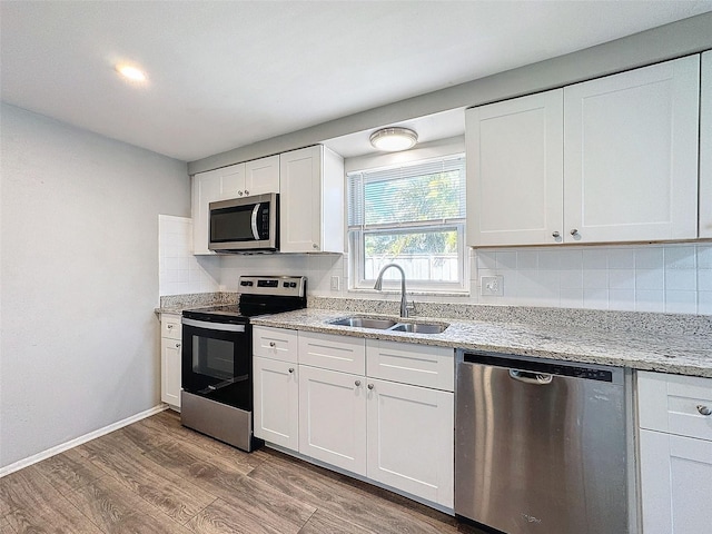 kitchen with decorative backsplash, appliances with stainless steel finishes, sink, light hardwood / wood-style flooring, and white cabinets