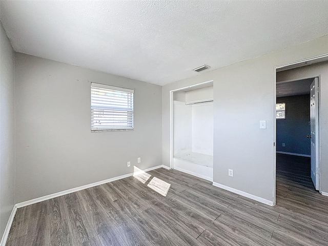 unfurnished bedroom featuring a textured ceiling, dark hardwood / wood-style floors, and a closet