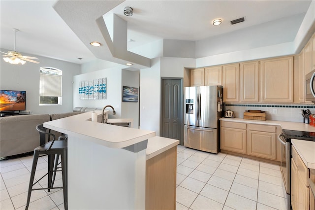 kitchen with a breakfast bar, sink, ceiling fan, an island with sink, and stainless steel appliances