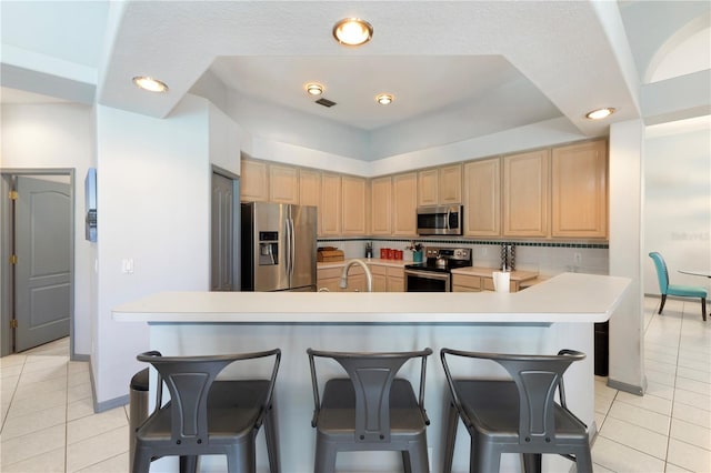 5211 Karlsburg Pl, Palm Harbor, FL 34685 - kitchen featuring appliances with stainless steel finishes, light tile patterned flooring, light brown cabinetry, a breakfast bar, and light countertops