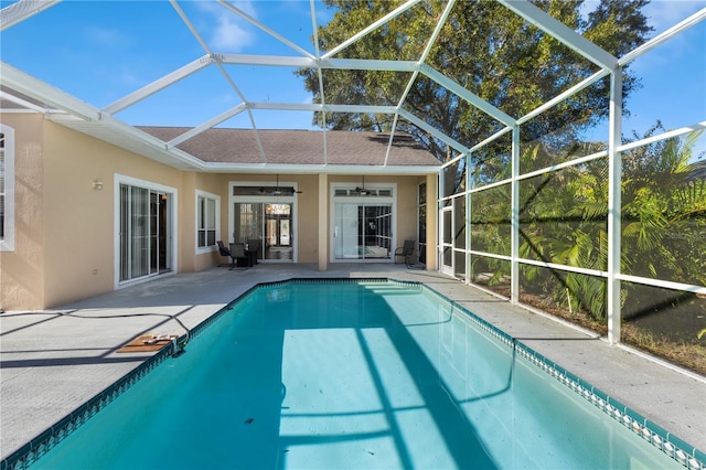 view of swimming pool with glass enclosure, ceiling fan, and a patio area