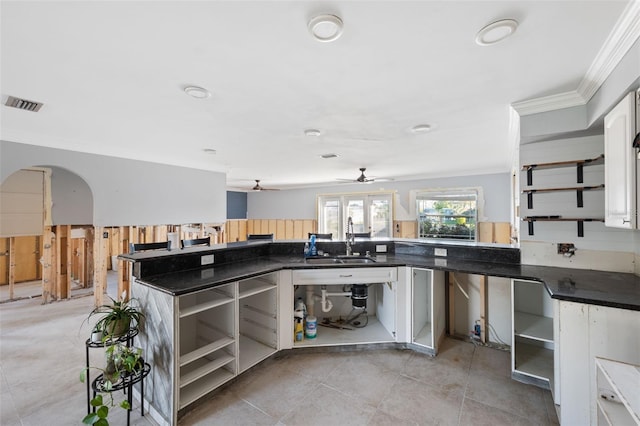 kitchen featuring kitchen peninsula, ornamental molding, ceiling fan, sink, and white cabinetry