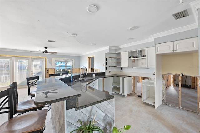 kitchen with kitchen peninsula, ceiling fan, crown molding, sink, and white cabinetry