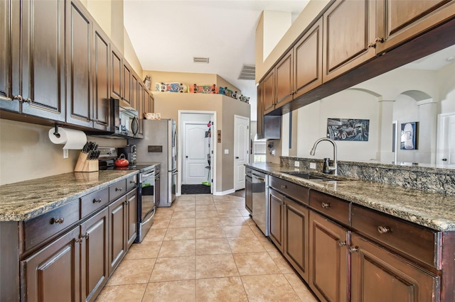 kitchen with dark brown cabinetry, sink, stainless steel appliances, dark stone counters, and light tile patterned floors