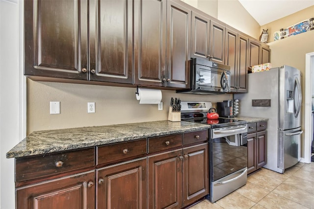 kitchen with dark brown cabinetry, dark stone counters, vaulted ceiling, light tile patterned flooring, and appliances with stainless steel finishes