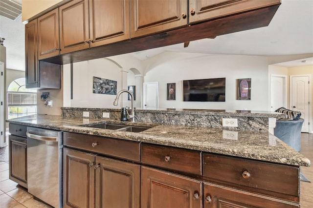 kitchen with stainless steel dishwasher, dark stone counters, sink, light tile patterned floors, and lofted ceiling