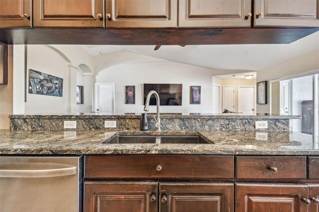 kitchen with stainless steel dishwasher, vaulted ceiling, dark stone counters, and sink