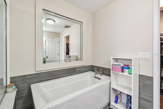 bathroom with a tub to relax in, a textured ceiling, and tile walls