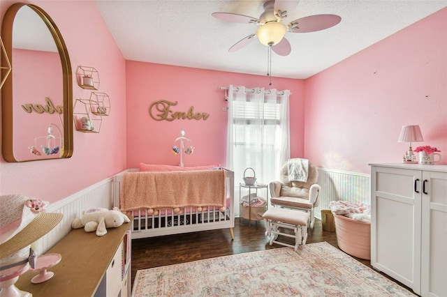 bedroom with ceiling fan, dark hardwood / wood-style flooring, and a nursery area