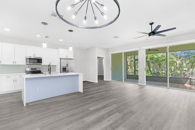 kitchen with hanging light fixtures, stainless steel appliances, wood-type flooring, a kitchen island with sink, and white cabinets