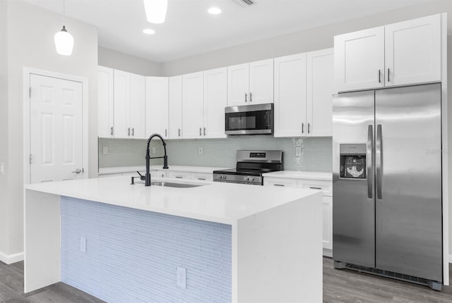 kitchen with pendant lighting, a kitchen island with sink, sink, white cabinetry, and stainless steel appliances