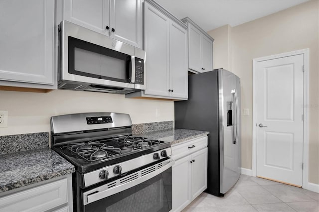 kitchen with light tile patterned flooring, appliances with stainless steel finishes, and dark stone counters