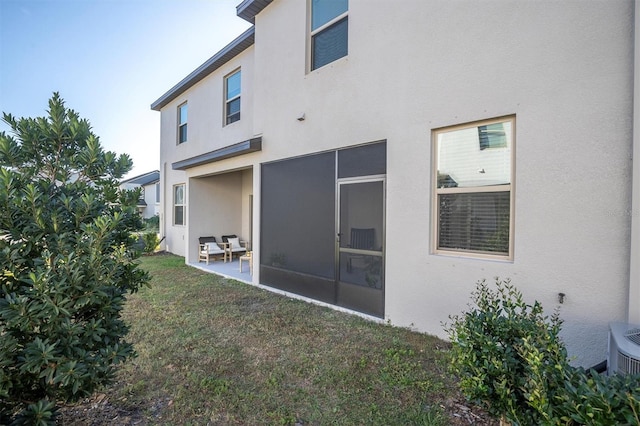 rear view of property featuring a lawn, a sunroom, and a patio