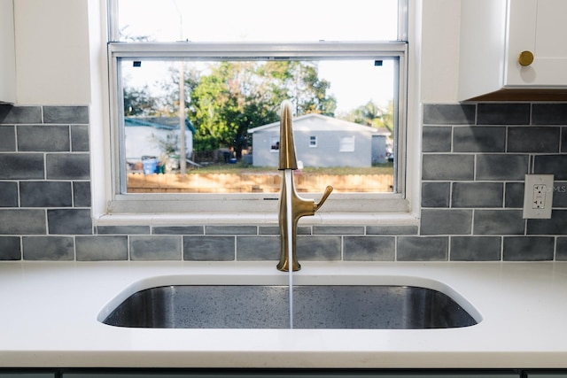 interior details with decorative backsplash, white cabinetry, and sink