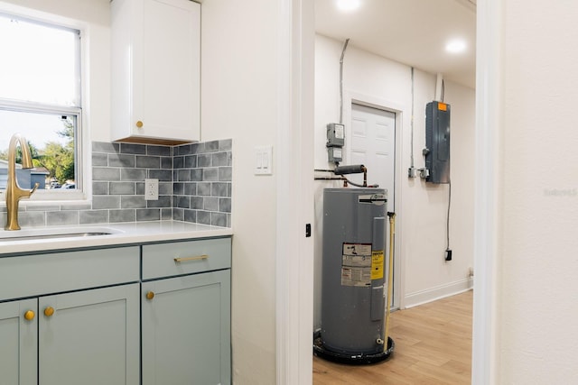 kitchen with backsplash, electric panel, sink, water heater, and light hardwood / wood-style floors