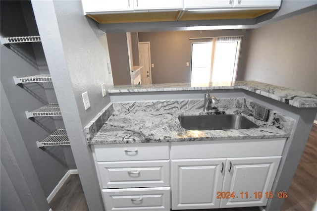 kitchen with light stone countertops, sink, dark hardwood / wood-style flooring, kitchen peninsula, and white cabinets