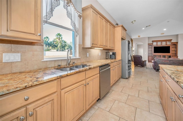 kitchen with appliances with stainless steel finishes, open floor plan, light stone countertops, a sink, and light tile patterned flooring