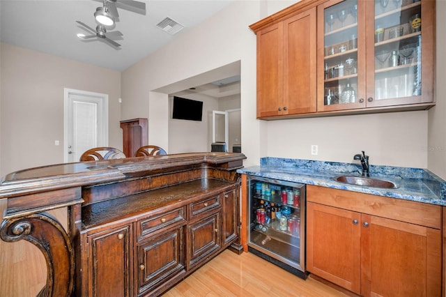 kitchen with light wood finished floors, beverage cooler, visible vents, dark stone counters, and a sink