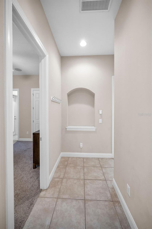 hallway with carpet floors, visible vents, baseboards, and tile patterned floors