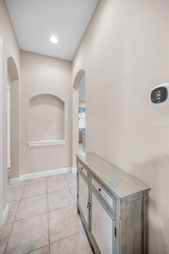 hallway with light tile patterned floors, baseboards, and arched walkways