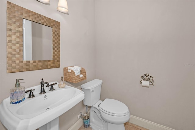 bathroom featuring toilet, tile patterned flooring, baseboards, and a sink