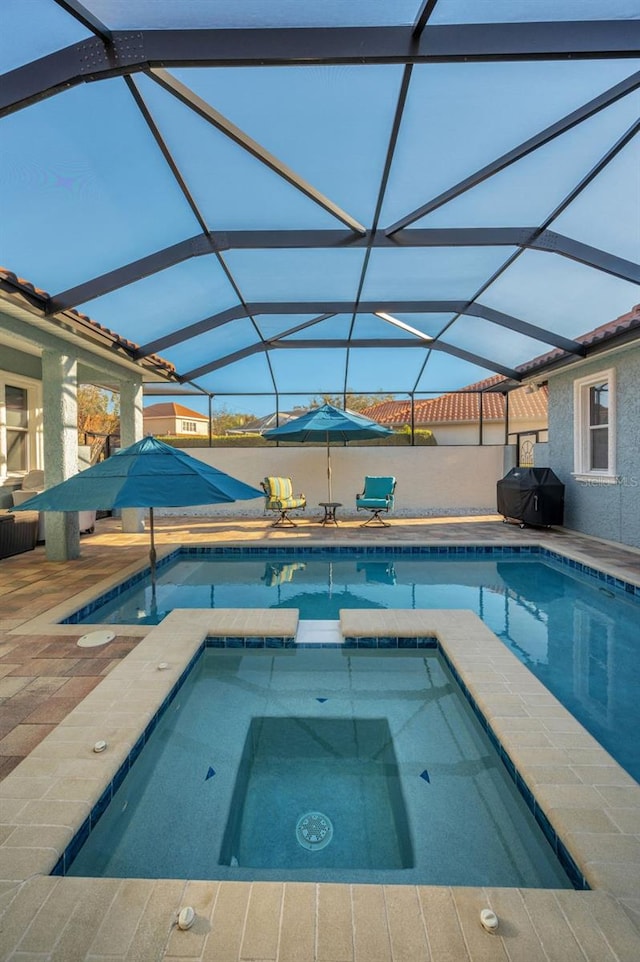 view of swimming pool with a patio area, a pool with connected hot tub, glass enclosure, and grilling area