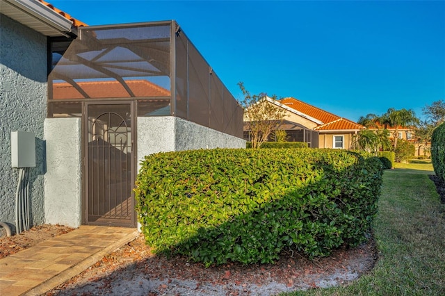 view of side of property with a tiled roof, a lawn, a lanai, and stucco siding