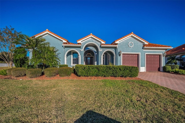 mediterranean / spanish home with decorative driveway, a tile roof, stucco siding, a front yard, and a garage