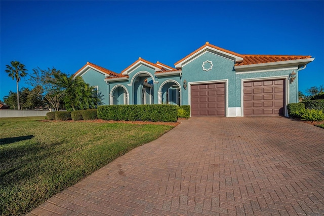 mediterranean / spanish-style house featuring a garage, a front lawn, decorative driveway, and a tile roof