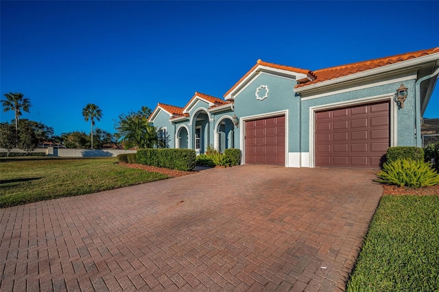 mediterranean / spanish home with a garage, a tile roof, decorative driveway, and stucco siding